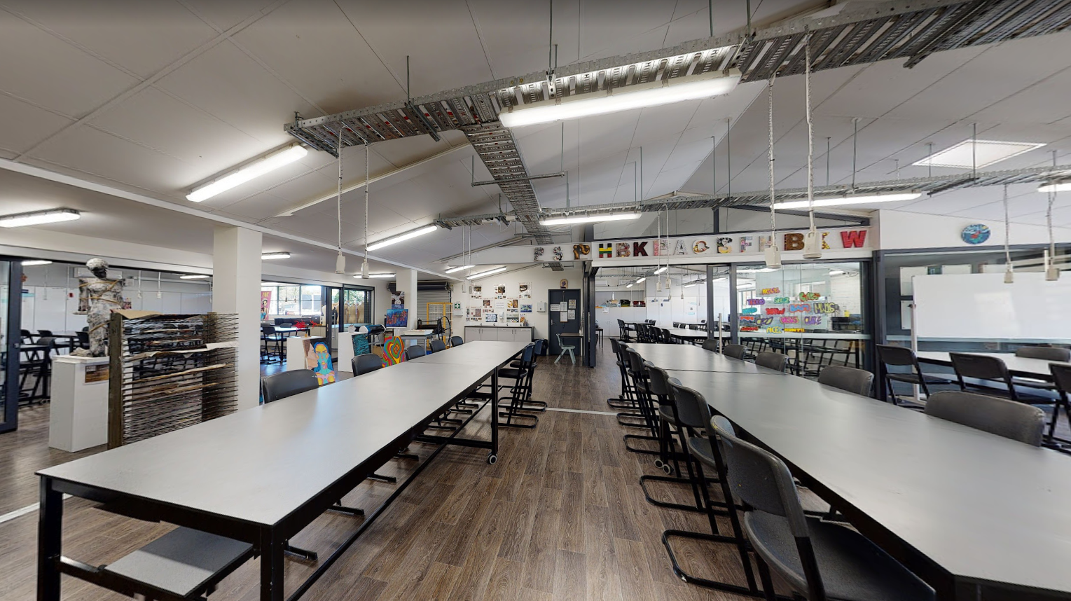Spacious art room with long work tables, stools, overhead lighting and creative materials displayed around the room