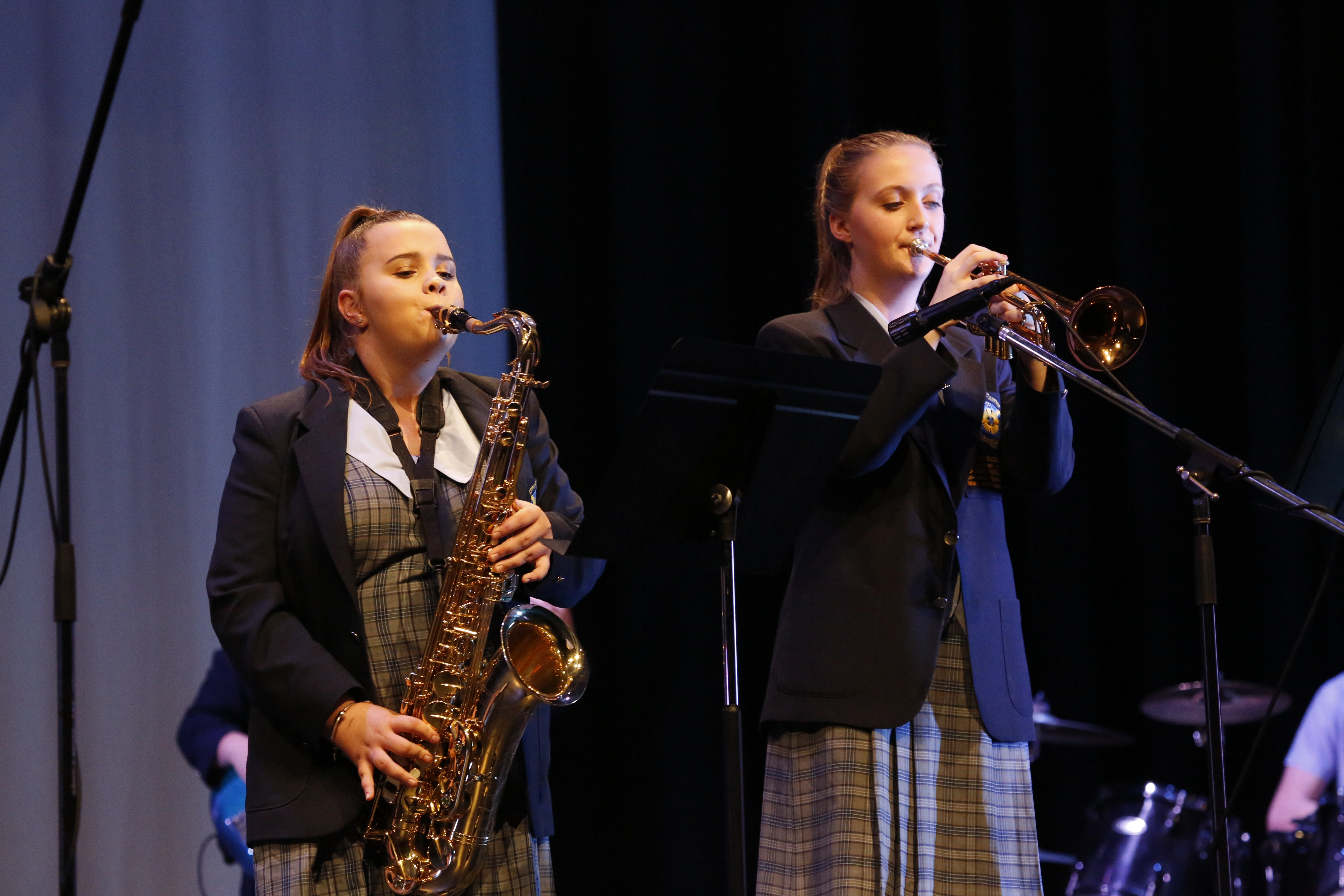 Two students in school uniforms performing on saxophone and trumpet on stage