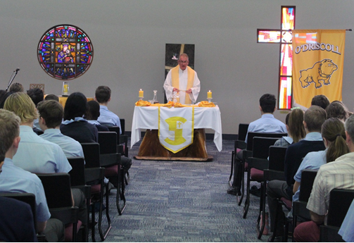 Group seated in a chapel watching a person standing at an altar with O’Driscoll House banners displayed
