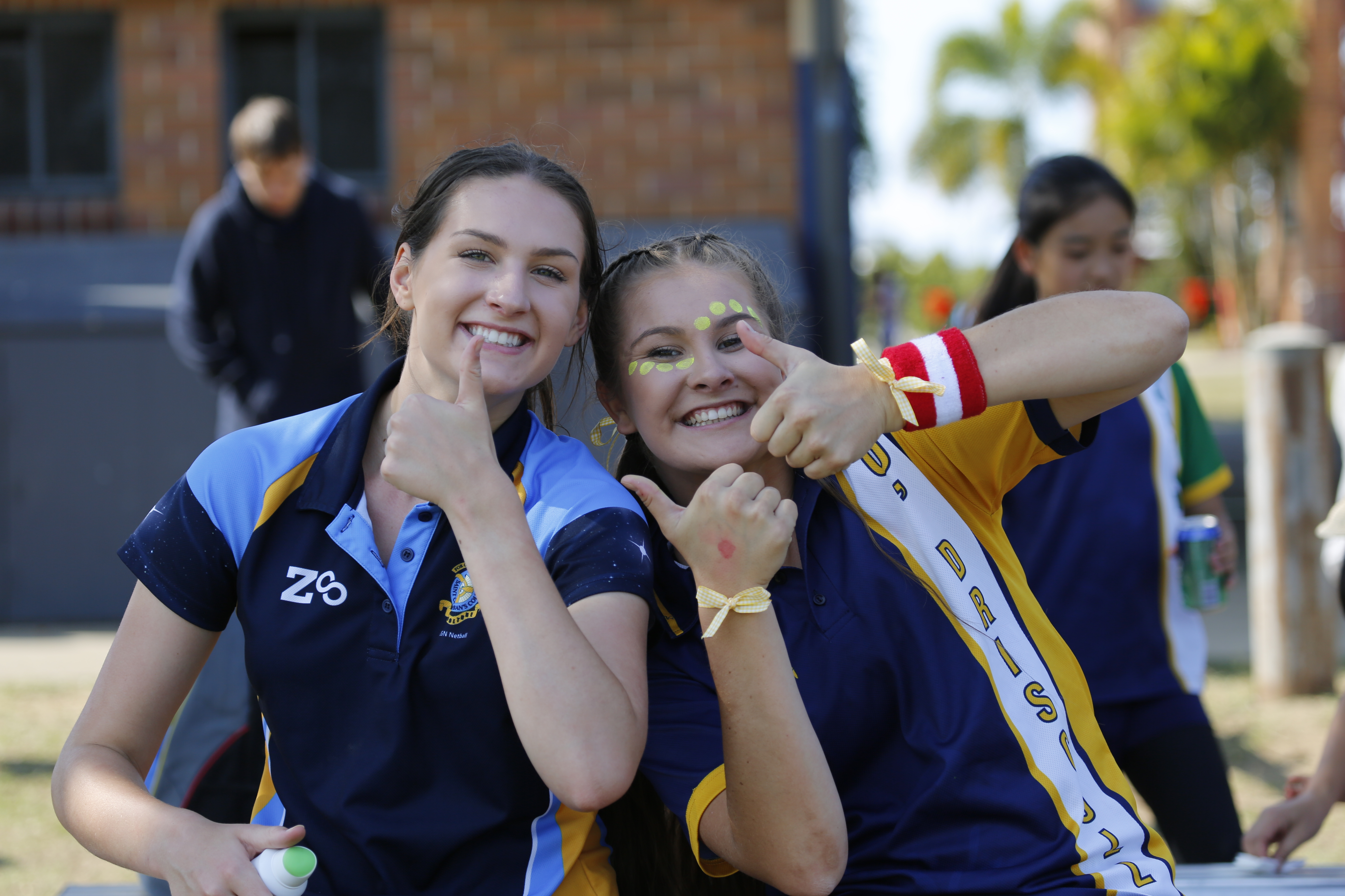 Two students sitting outdoors giving a thumbs‑up gesture