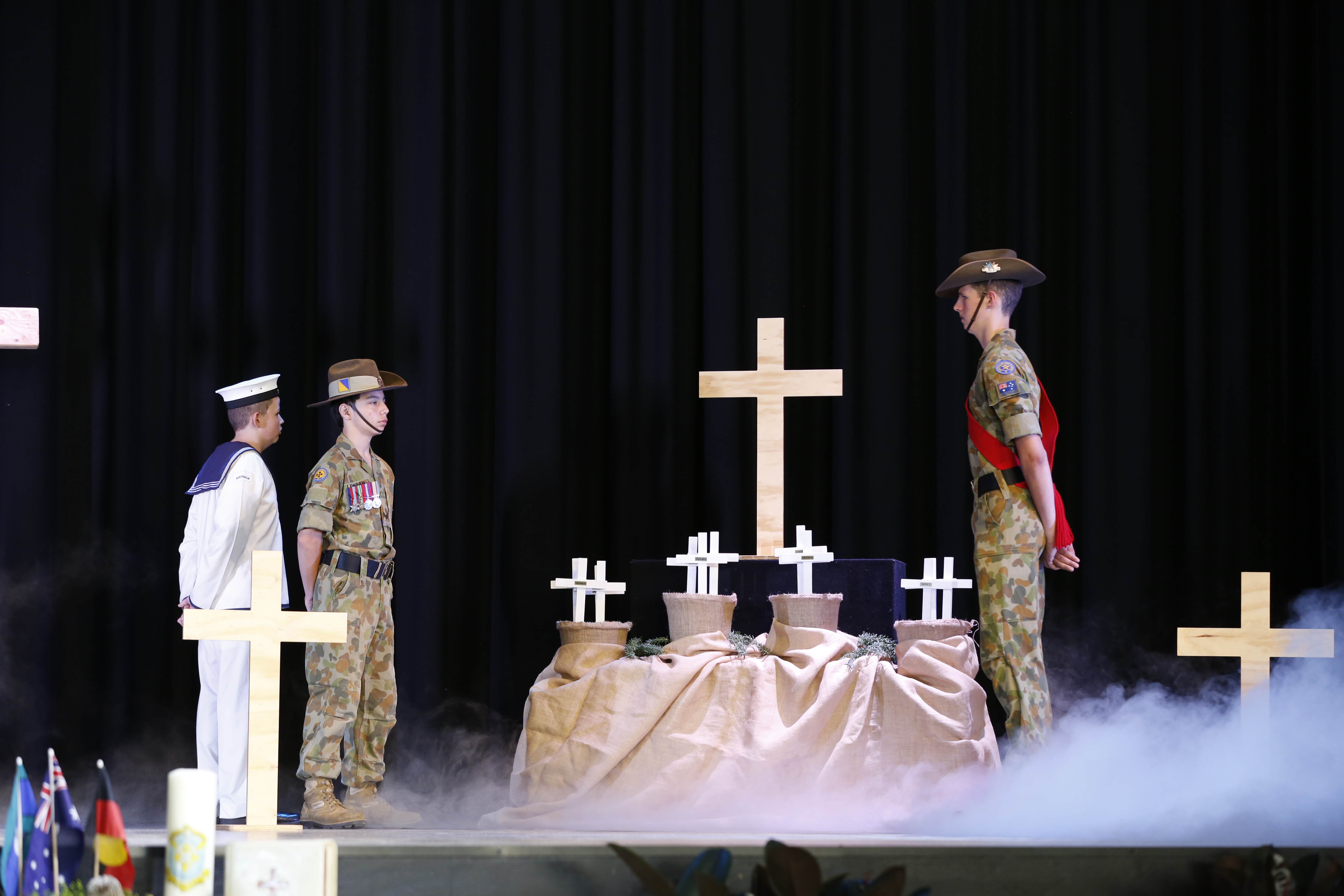 Students in ceremonial uniforms standing beside wooden crosses on a staged display