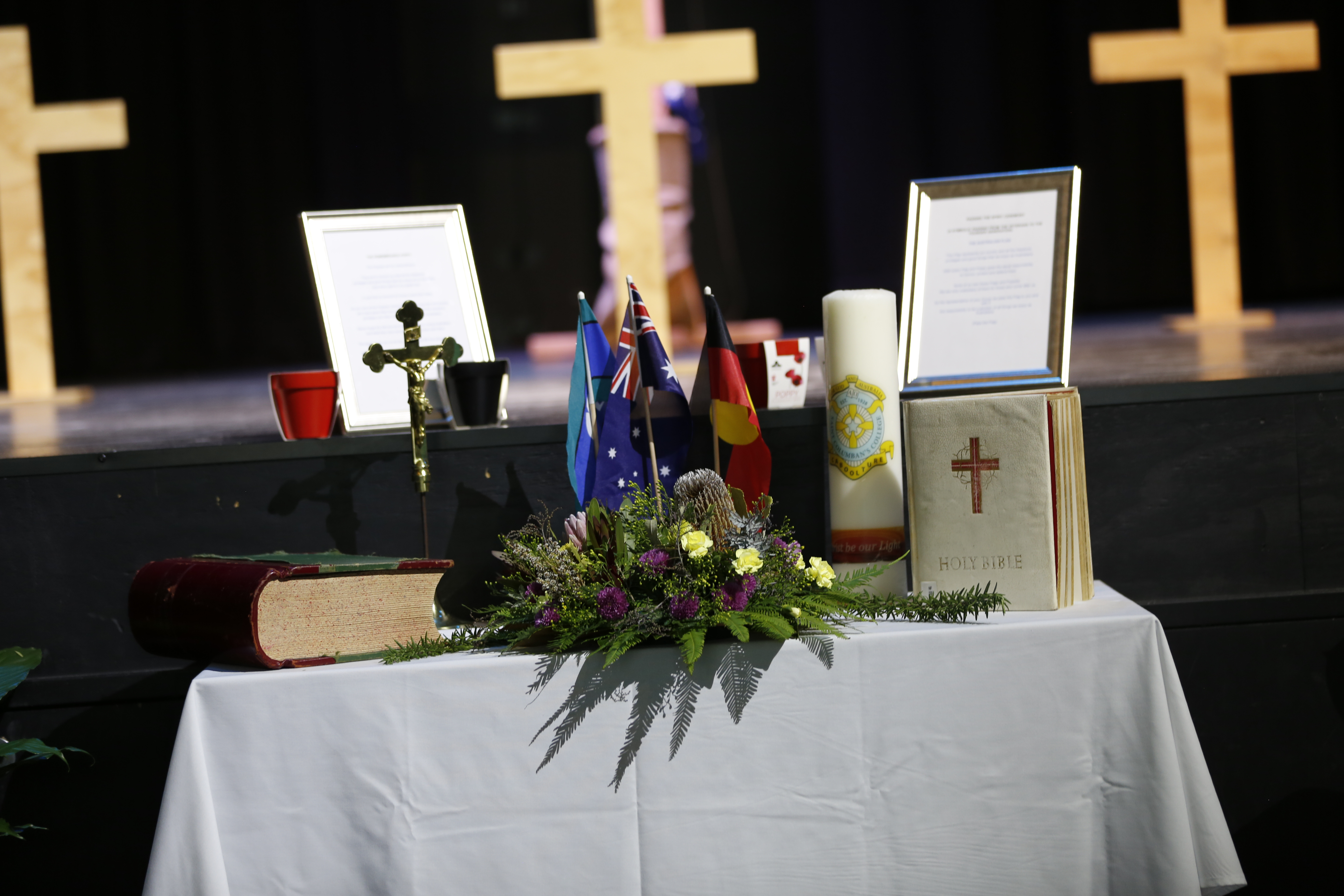 Table with flags, a floral arrangement, candles, books, and documents in front of wooden crosses
