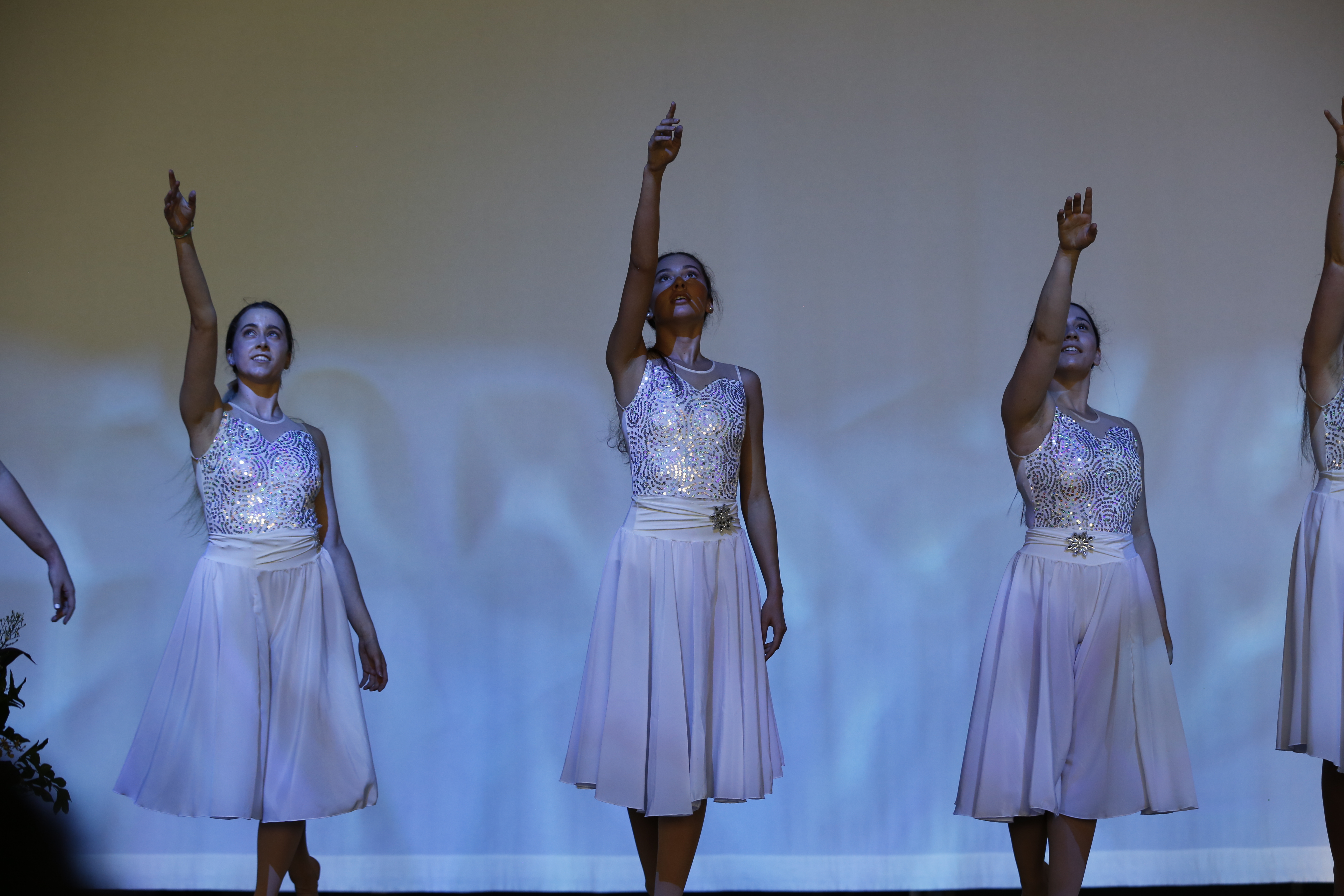 Group of performers in matching light‑coloured dresses on stage with arms raised