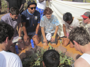 Group of students sitting in a circle outdoors around a smoking leaf arrangement