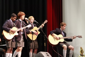 Students in school uniforms playing acoustic guitars on stage