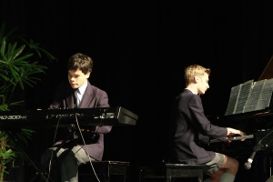 Two students in school uniforms playing keyboard and piano on stage
